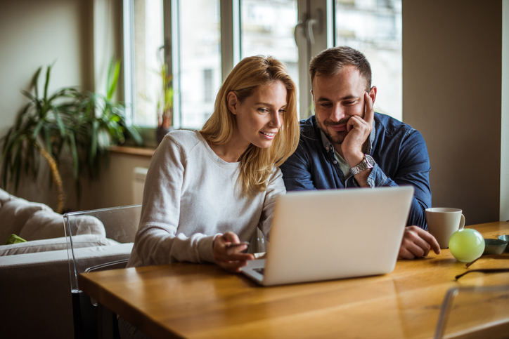 couple sitting at a table looking at a laptop for financial insights